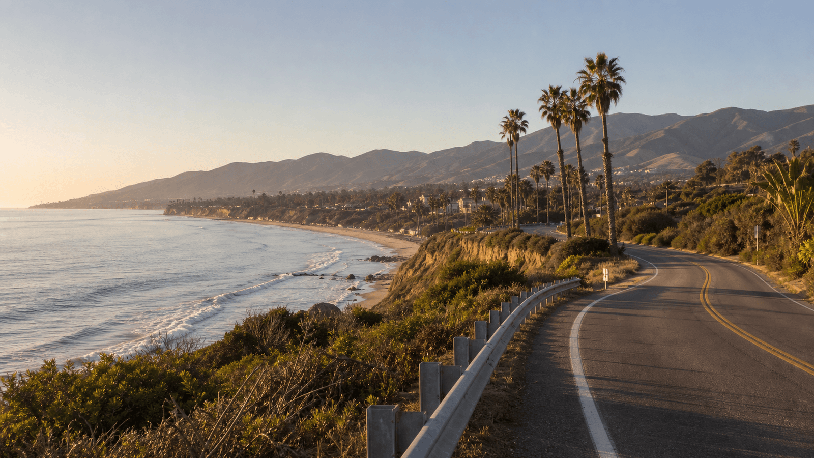 Coastal road beside a beach and palms below brown hills