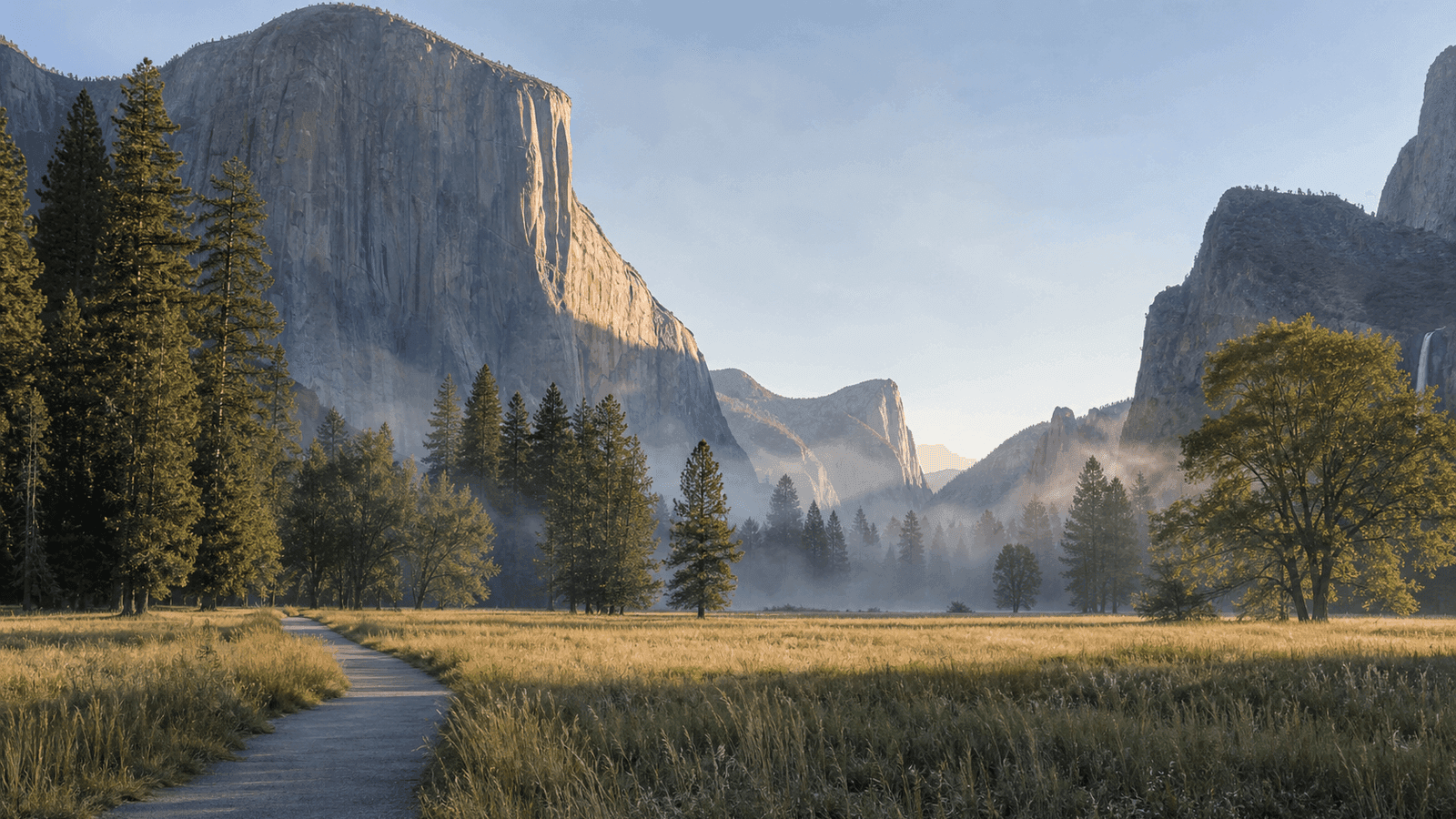 Path across a meadow below tall granite walls