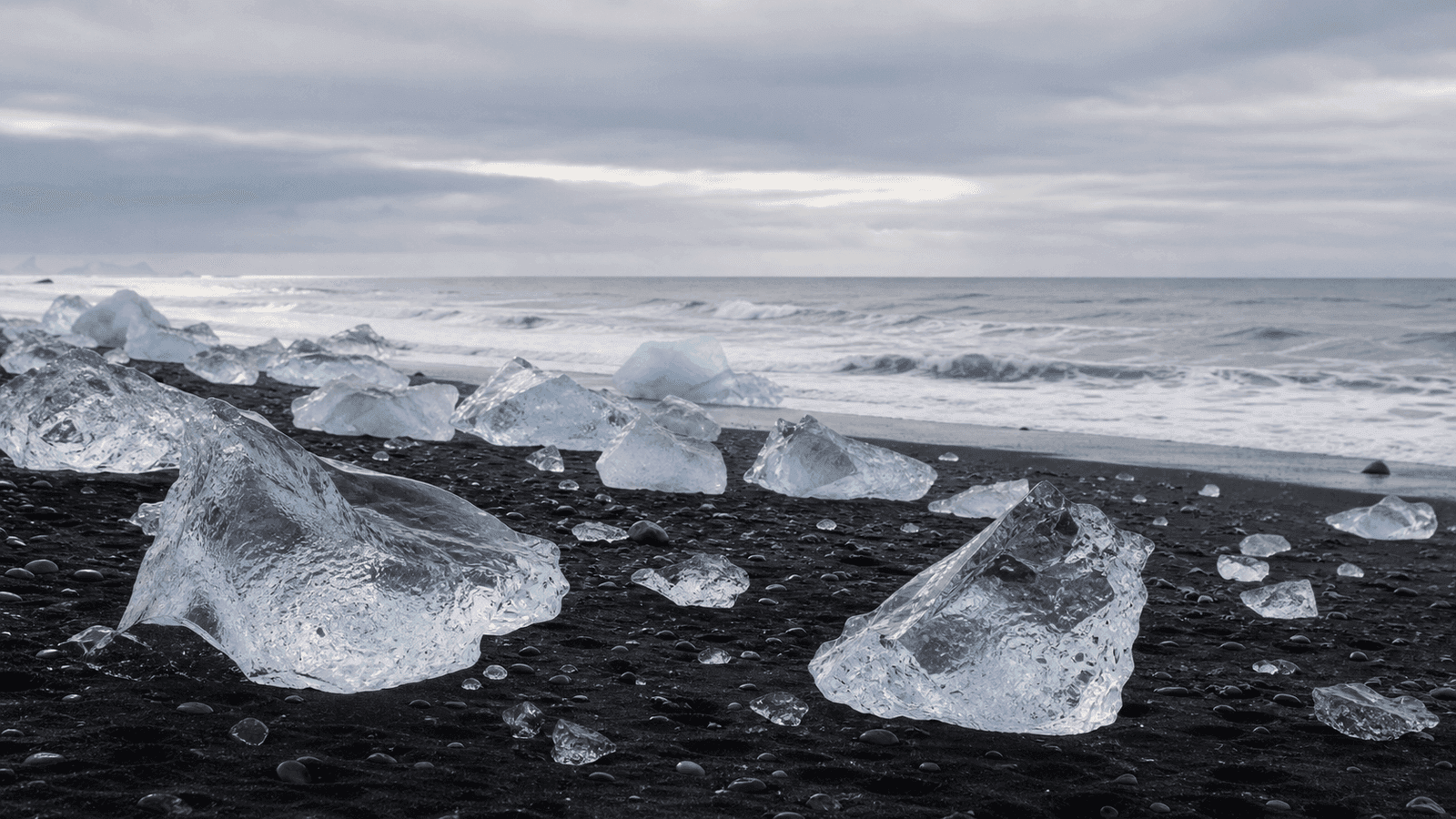 Ice pieces on black sand beside the surf