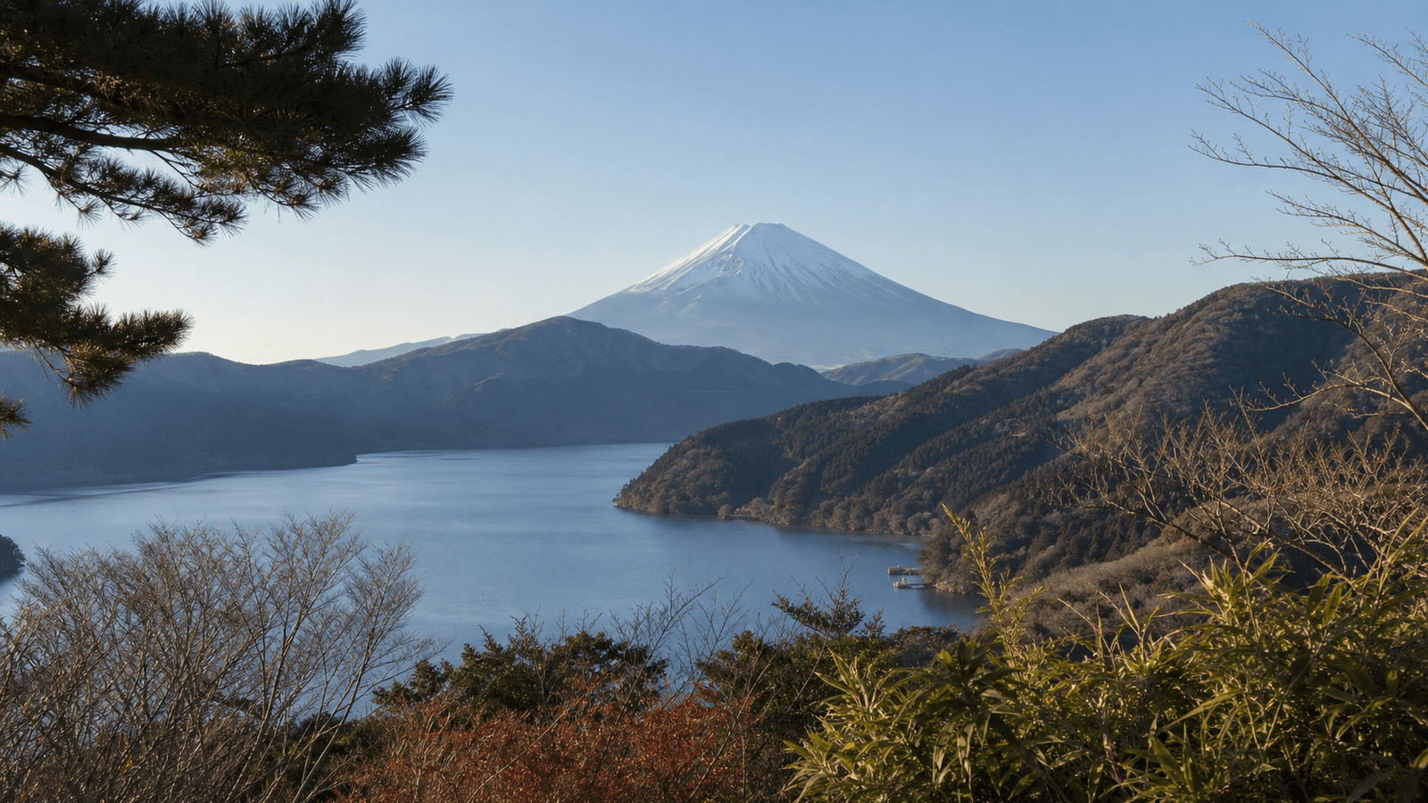 Snow-covered conical mountain beyond a lake and wooded hills