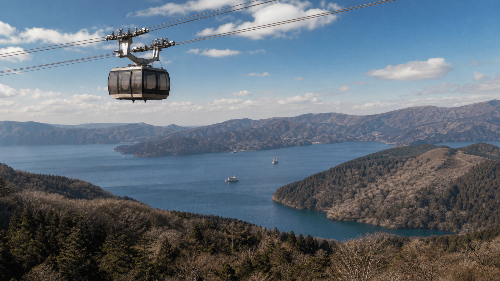 Ropeway gondola above wooded hills and a lake with sightseeing ships