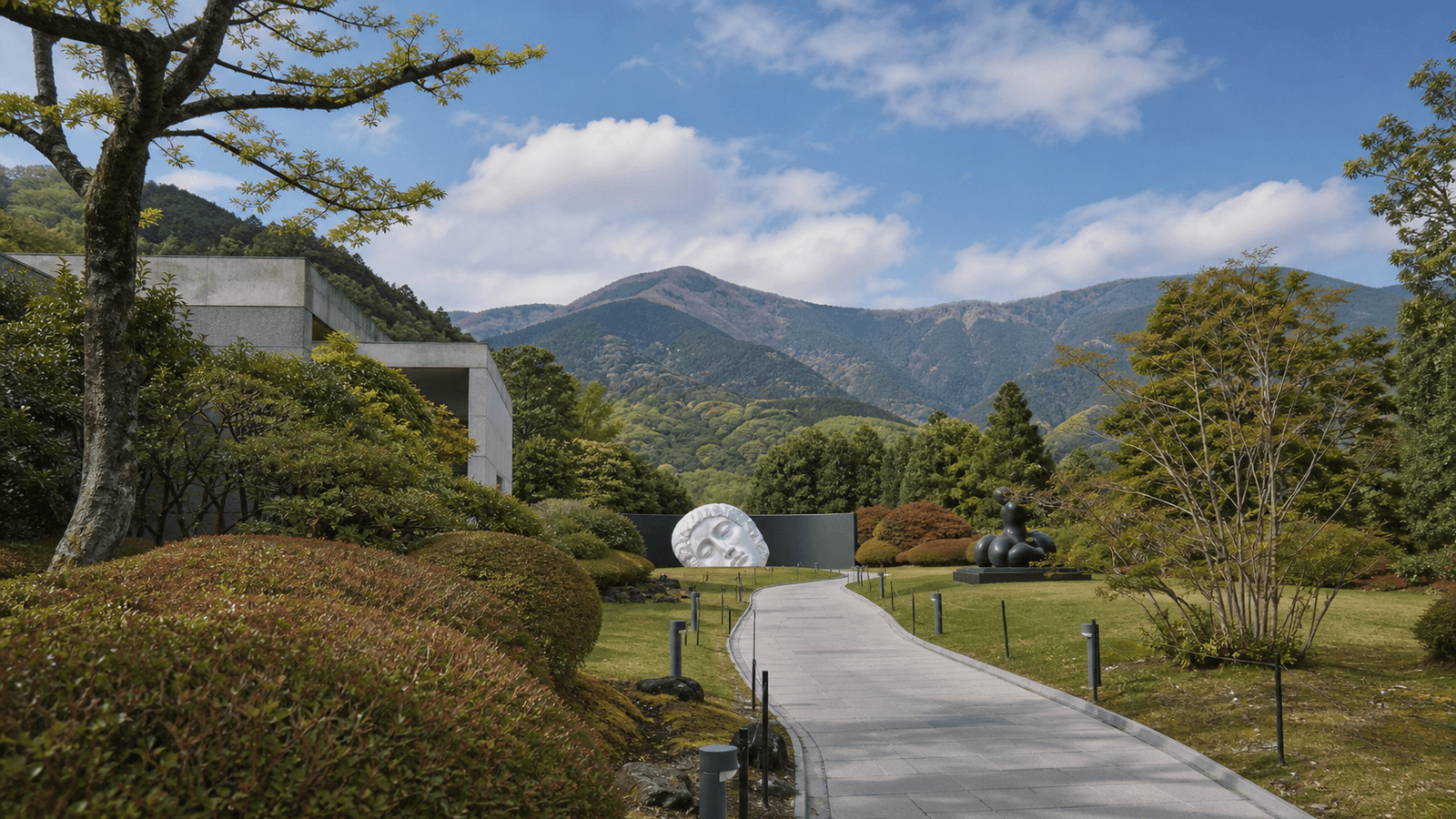 Path through a planted sculpture garden with a face sculpture and mountains beyond