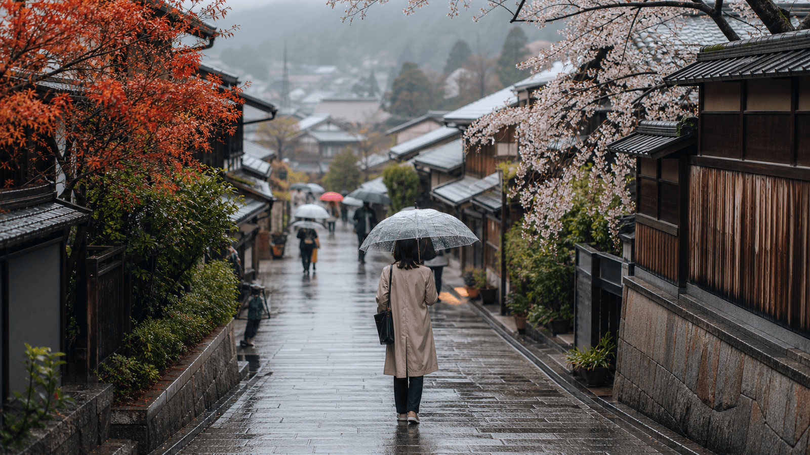 People carrying umbrellas along a street of wooden houses beneath blossoms and red leaves