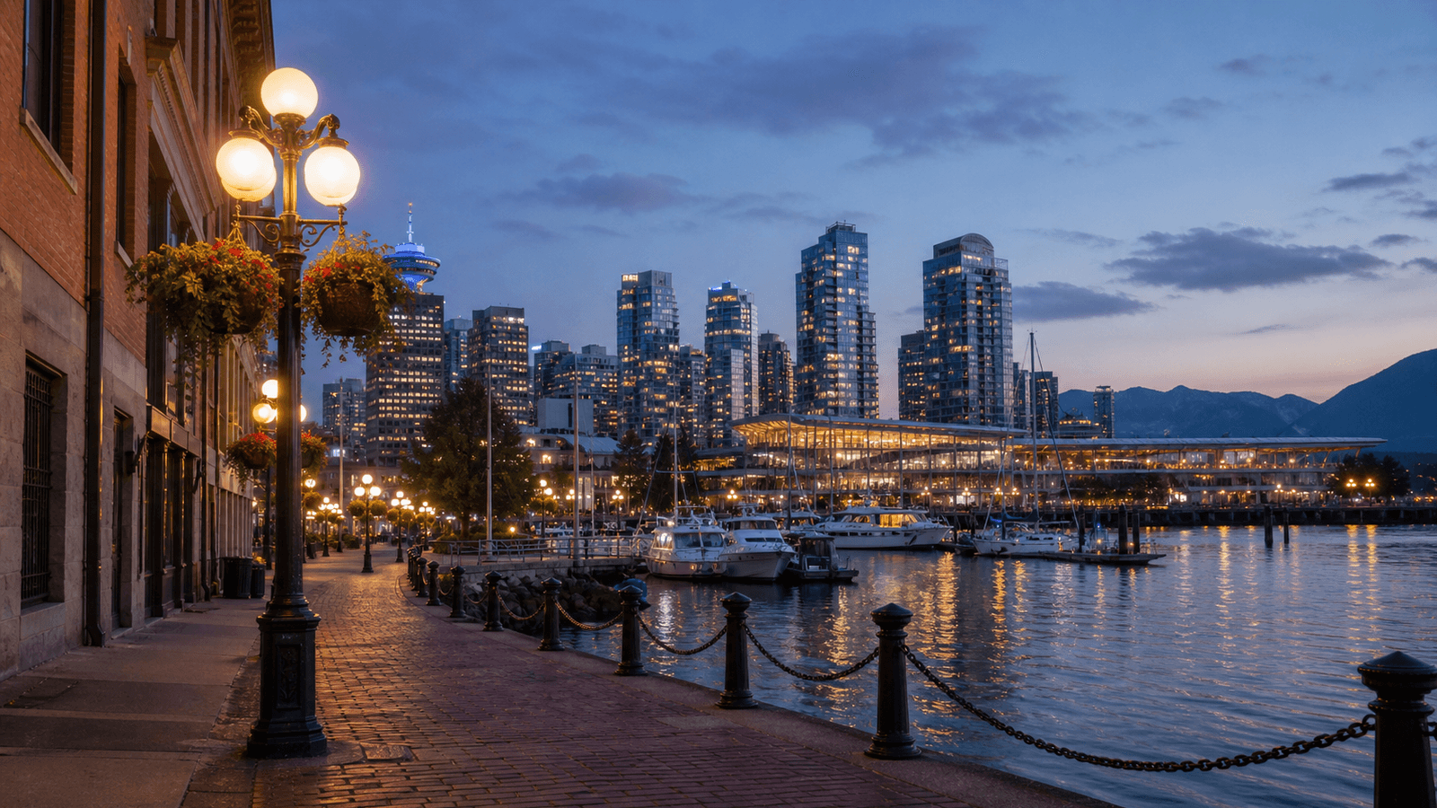 Lit waterfront promenade with a harbour and high-rises at dusk