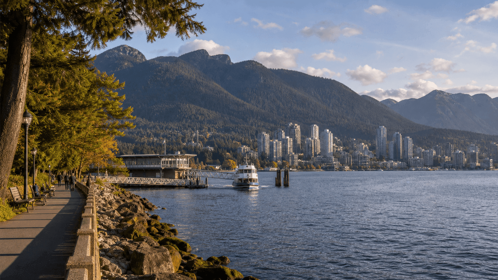 Shore path overlooking an inlet, buildings and forested mountains